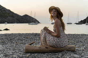 Young woman journalising, sitting on the beach at sunset - AFVF03935