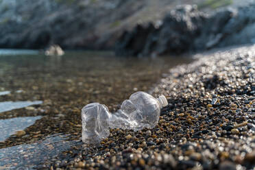 Leere Plastikflasche liegt am steinigen Strand am Meer - AFVF03943