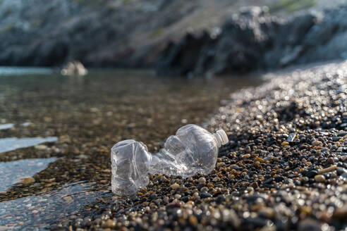 Empty plastic bottle lying on stony beach at seaside - AFVF03943