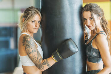 Portrait of two women with boxing gloves at sandbag in gym - DLTSF00093