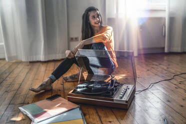 Junge Frau sitzt zu Hause auf dem Boden mit einem Plattenspieler - RIBF00988