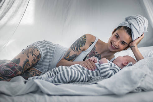 Porträt einer lächelnden, tätowierten jungen Frau mit ihrem Baby im Himmelbett - RIBF00999