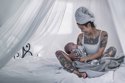 Happy tattooed young woman with her baby in canopy bed - RIBF01001