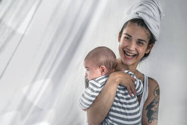 Glückliche tätowierte junge Frau hält ihr Baby - RIBF01004