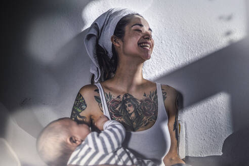 Glückliche tätowierte junge Frau hält ihr Baby zu Hause - RIBF01018