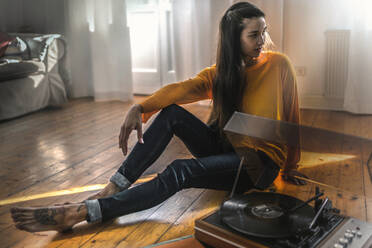 Young woman sitting on the floor at home with a record player - RIBF01023