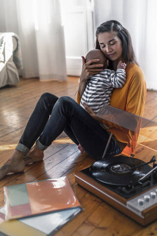 Mutter mit Baby sitzt zu Hause auf dem Boden mit einem Plattenspieler, lizenzfreies Stockfoto