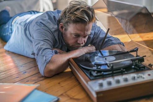 Man lying on the floor at home with a record player - RIBF01029