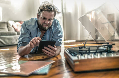 Mann auf dem Boden liegend zu Hause mit Tablet und Plattenspieler, lizenzfreies Stockfoto