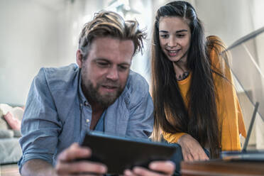 Paar liegt zu Hause auf dem Boden und schaut auf ein Tablet - RIBF01034