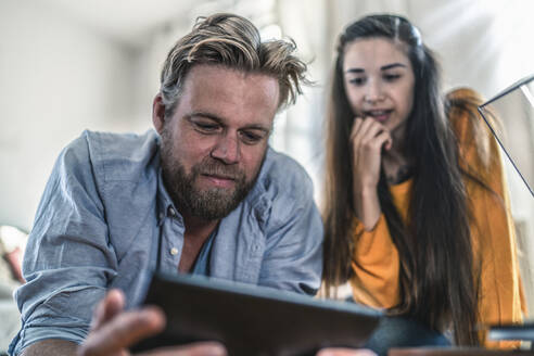 Paar liegt zu Hause auf dem Boden und schaut auf ein Tablet - RIBF01035