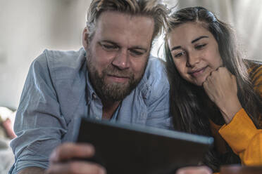 Paar liegt zu Hause auf dem Boden und schaut auf ein Tablet - RIBF01036