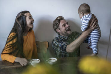 Happy family with baby sitting at wooden table at home - RIBF01041