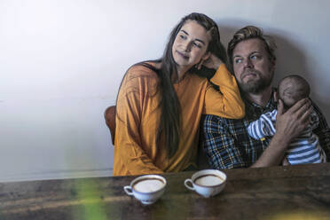 Relaxed family with baby sitting at wooden table at home - RIBF01042