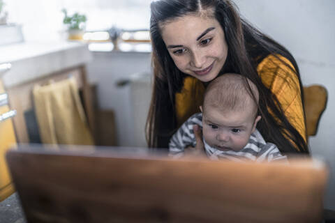 Mother with baby using laptop on kitchen table stock photo