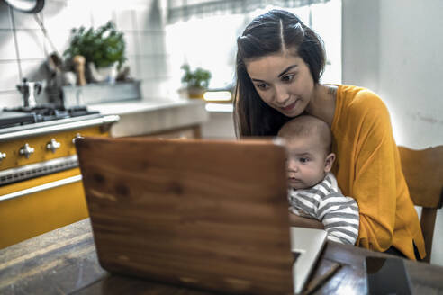 Mutter mit Baby am Laptop auf dem Küchentisch - RIBF01048