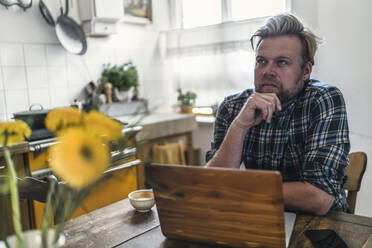 Man using laptop on kitchen table - RIBF01049