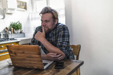 Man using laptop on kitchen table - RIBF01050