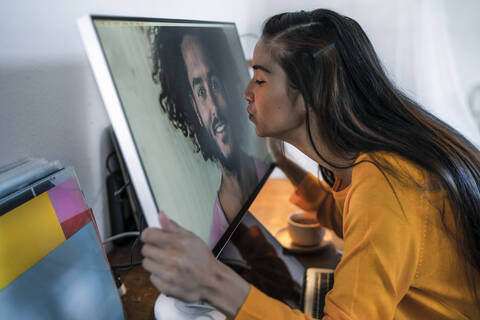 Junge Frau küsst Mann auf Computerbildschirm, lizenzfreies Stockfoto