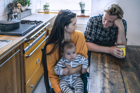 Serious family with baby sitting at kitchen table at home stock photo