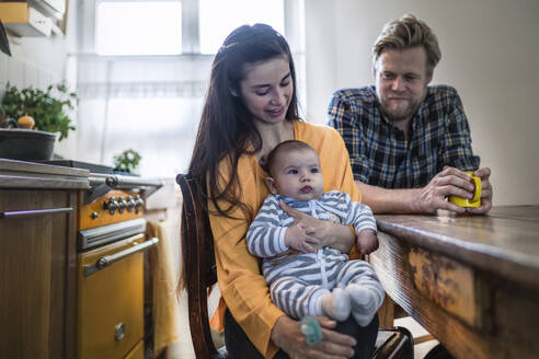 Familie mit Baby sitzt am Küchentisch zu Hause - RIBF01070