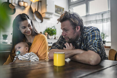 Familie mit Baby sitzt am Küchentisch zu Hause - RIBF01071