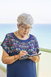 Ältere Frau benutzt ein Tablet auf einer Terrasse - DLTSF00114