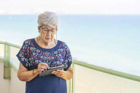 Ältere Frau benutzt ein Tablet auf einer Terrasse, lizenzfreies Stockfoto