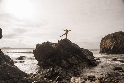 Woman wearing yellow rain jacket standing at rocky beach stock photo