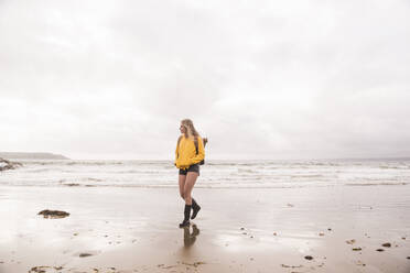 Woman wearing yellow rain jacket walking at the beach - UUF18984