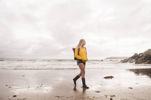 Frau mit gelber Regenjacke beim Spaziergang am Strand - UUF18985