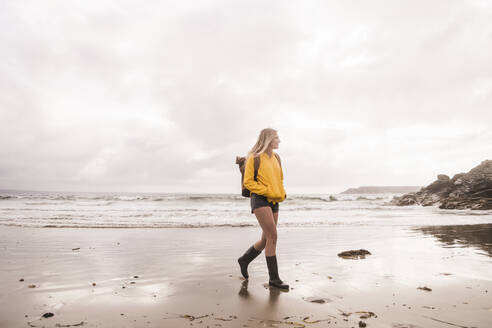 Woman wearing yellow rain jacket walking at the beach - UUF18985