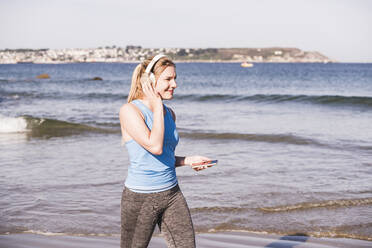 Joggerin am Strand, mit Smartphone und Kopfhörern - UUF19004