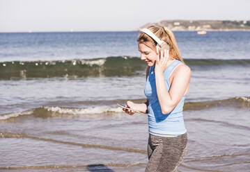 Joggerin am Strand, mit Smartphone und Kopfhörern - UUF19005