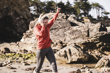 Weibliche Joggerin tanzt am Strand mit Kopfhörern - UUF19008