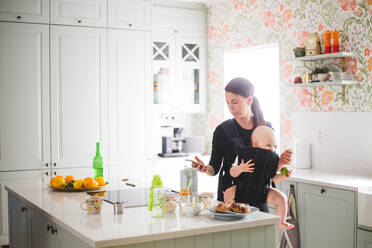 Mother using mobile phone while carrying daughter in kitchen at home - MASF13439