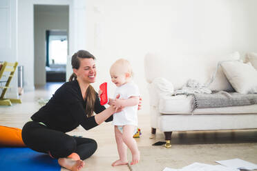 Cheerful working mother holding daughter while exercising in living room at home office - MASF13440