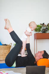 Side view of cheerful mother playing with daughter while lying in home office - MASF13441