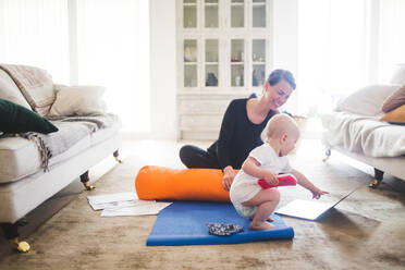 Lächelnde Mutter schaut auf ihre Tochter, die auf einen Laptop zeigt, während sie im Wohnzimmer Yoga übt - MASF13444