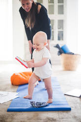 Female parent exercising on exercise mat while daughter playing with toy at home - MASF13445
