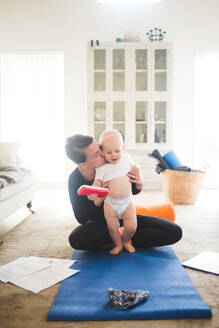 Eine Unternehmerin küsst ihre Tochter, während sie zu Hause im Wohnzimmer Yoga übt - MASF13447