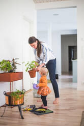 Modedesignerin und Tochter bei der Gartenarbeit, während sie zu Hause auf dem Hartholzboden stehen - MASF13454