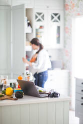 Arbeitende Mutter mit Tochter bei der Vorbereitung eines Blogs in der Küche zu Hause - MASF13462