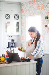 Berufstätige Mutter mit Tochter bei der Vorbereitung eines Foodblogs, während sie einen Laptop auf der Kücheninsel zu Hause benutzt - MASF13463