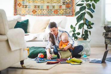 Multitasking-Mutter mit Stoffmustern und Tochter bei der Arbeit im heimischen Wohnzimmer in voller Länge - MASF13474