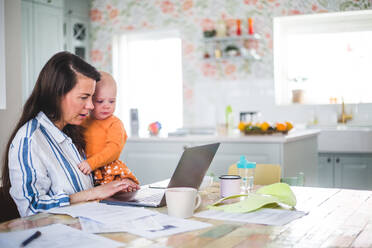 Unternehmerin mit liebender Tochter bei der Benutzung eines Laptops auf dem Esstisch im Büro zu Hause - MASF13482