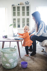 Porträt eines kleinen Mädchens mit einer vielbeschäftigten Mutter im Wohnzimmer eines Büros - MASF13485