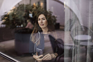 Businesswoman listening music while standing by window in office - MASF13502