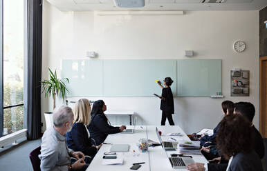 Kollegen konzentrieren sich auf eine Geschäftsfrau, die während einer Sitzung im Büro eine Präsentation hält - MASF13527