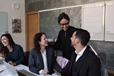 Lächelnde Geschäftsfrau im Gespräch mit fröhlichen Kollegen im Büro - MASF13531
